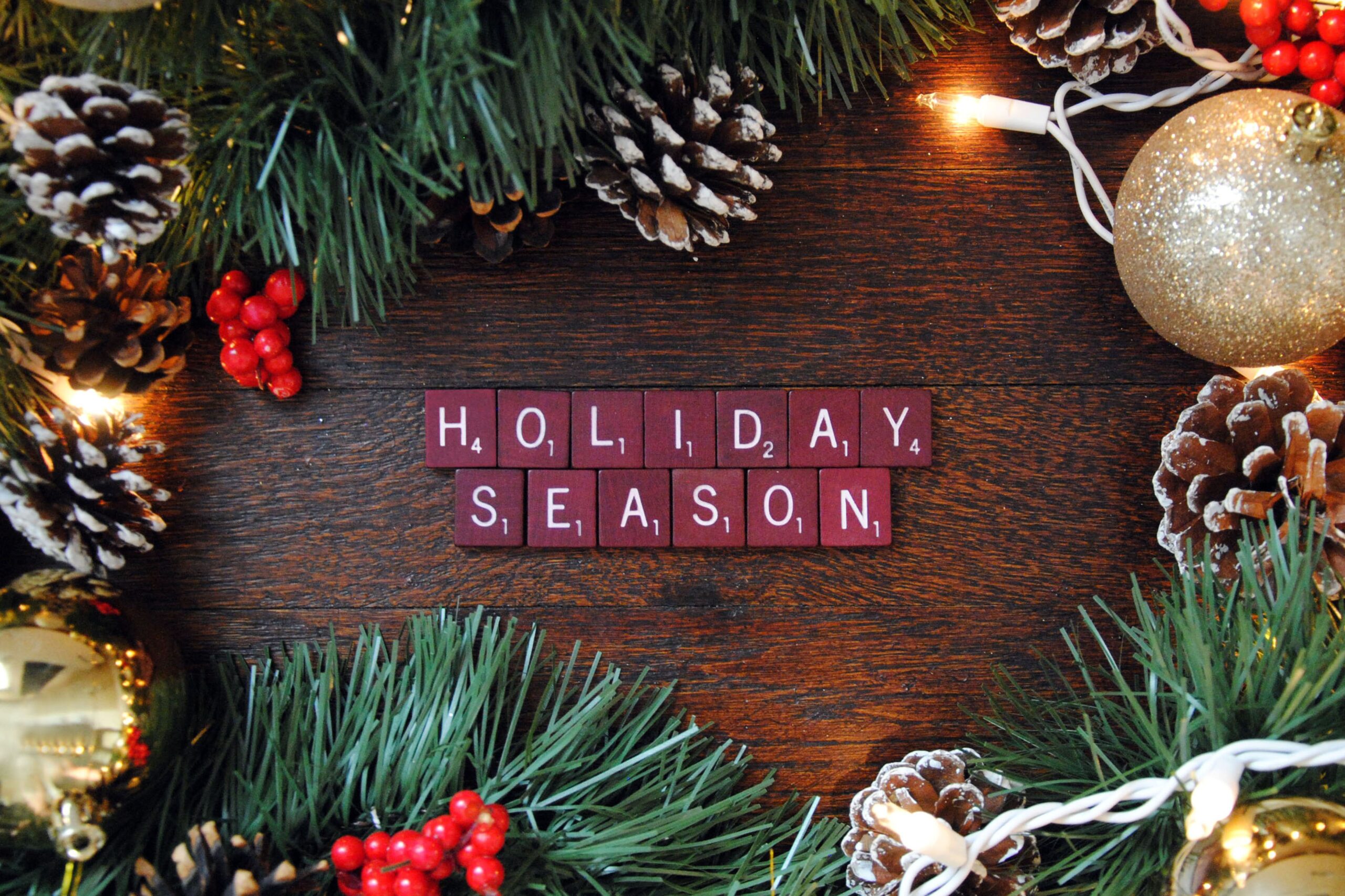 festive holiday image with pine cones, ornaments, white string lights, and letter blocks spelling holiday season